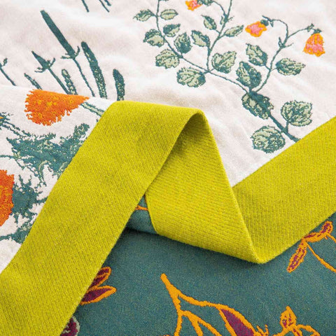 Close-up of Verdant Bloom cotton throw blanket fabric and green edge detail