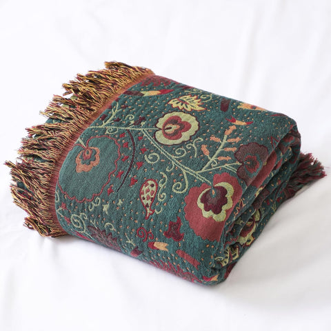 Folded vintage boho cotton throw blanket with fringed edges on white surface