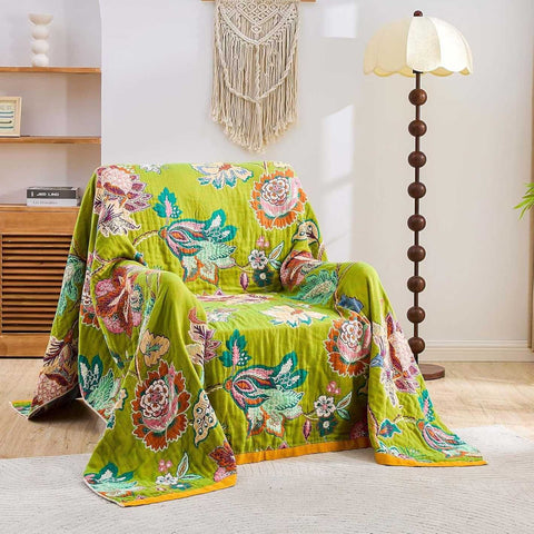 Vintage Garden Cotton Throw Blanket with warm floral patterns draped over a beige armchair in a cozy, bright living room setting