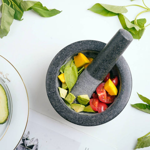 Top view of vintage marble mortar filled with fresh avocado, tomato, and leaves on white surface