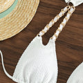 Detail of gold chain strap on white crinkle bikini top lying on wood background

