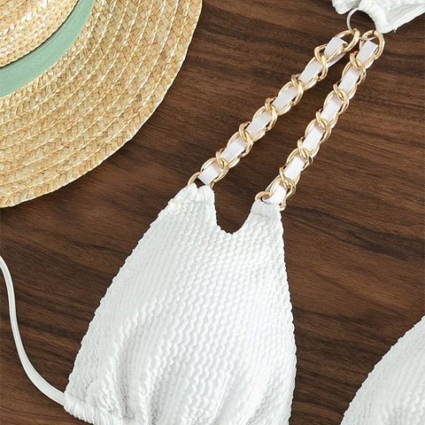 Detail of gold chain strap on white crinkle bikini top lying on wood background

