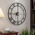 Large round wall clock with black frame and gold hands on a light gray wall.
