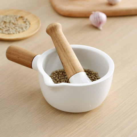 White ceramic mortar and pestle with wooden handle crushing peppercorns on wooden table