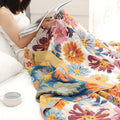 Woman reading a book while wrapped in Daisy Flower Cotton Blanket in a cozy bedroom setting