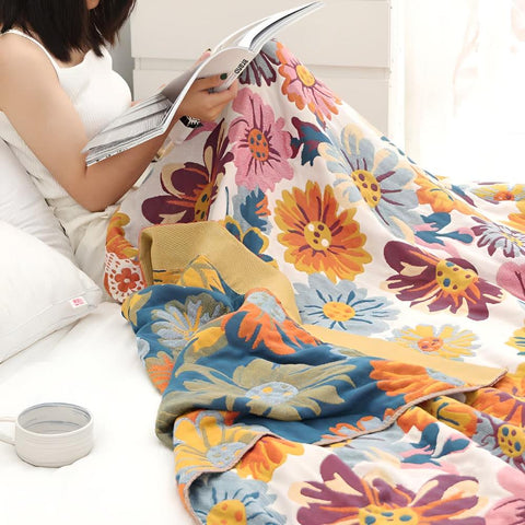 Woman reading a book while wrapped in Daisy Flower Cotton Blanket in a cozy bedroom setting