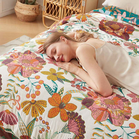 Woman peacefully resting on bohemian floral cotton throw blanket on bed in bright room.