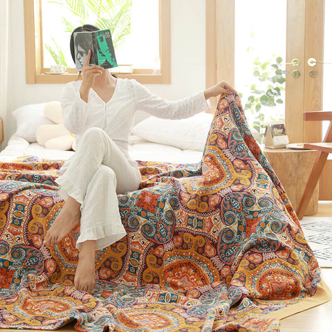 Woman lifting vibrant orange and blue boho quilt while sitting on bed