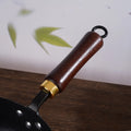 Close-up of a frying pan handle with wooden handle and gold accent on a wooden surface.