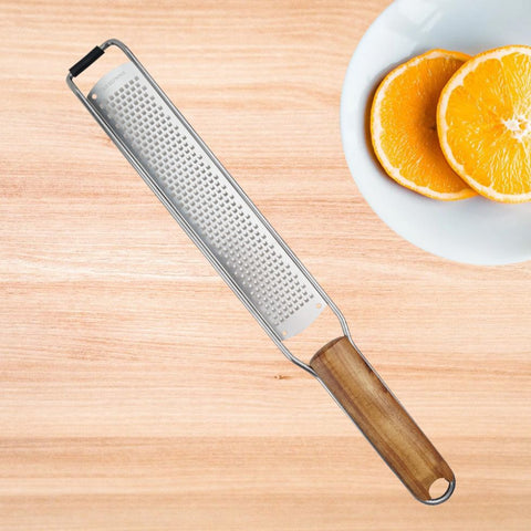 Wooden handle stainless steel grater with orange slices on a white plate on wooden table