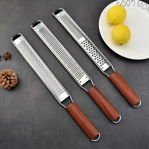 Three wooden handle stainless steel graters with different grating sizes on a dark surface with two lemons on a white plate nearby